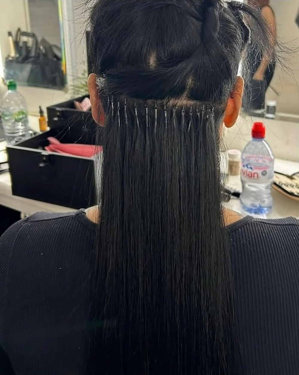 Neat rows of extension bonds on long dark hair, mid-application